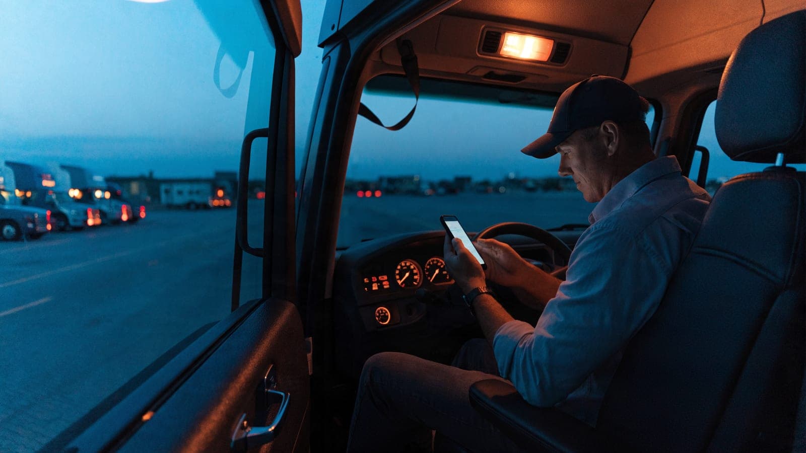 Owner-operator checking a freight broker's credit on a smartphone in the cab of a semi-truck at dusk.