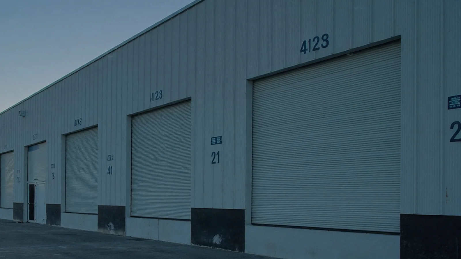A receding row of closed roll-up dock doors along a warehouse wall at first light.